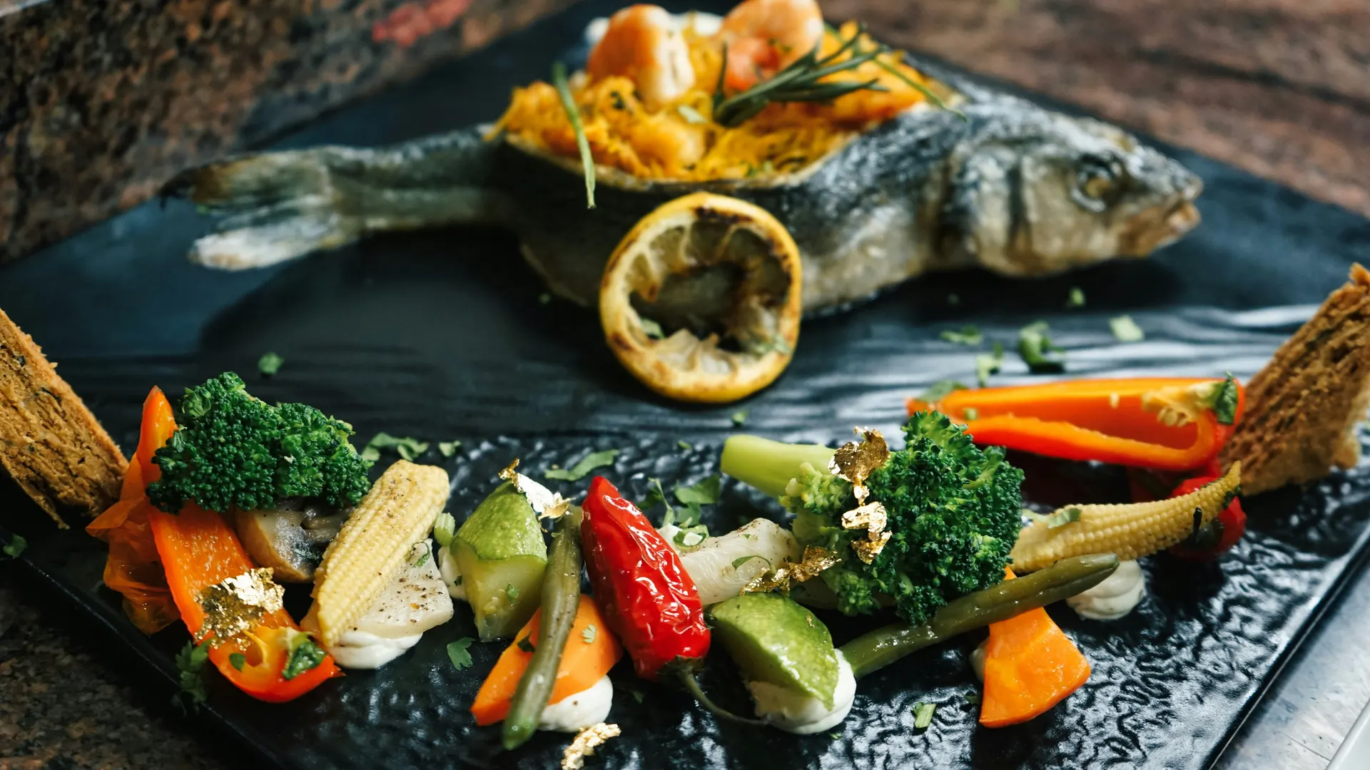 Whole grilled fish with lemon and vegetables on a dark plate