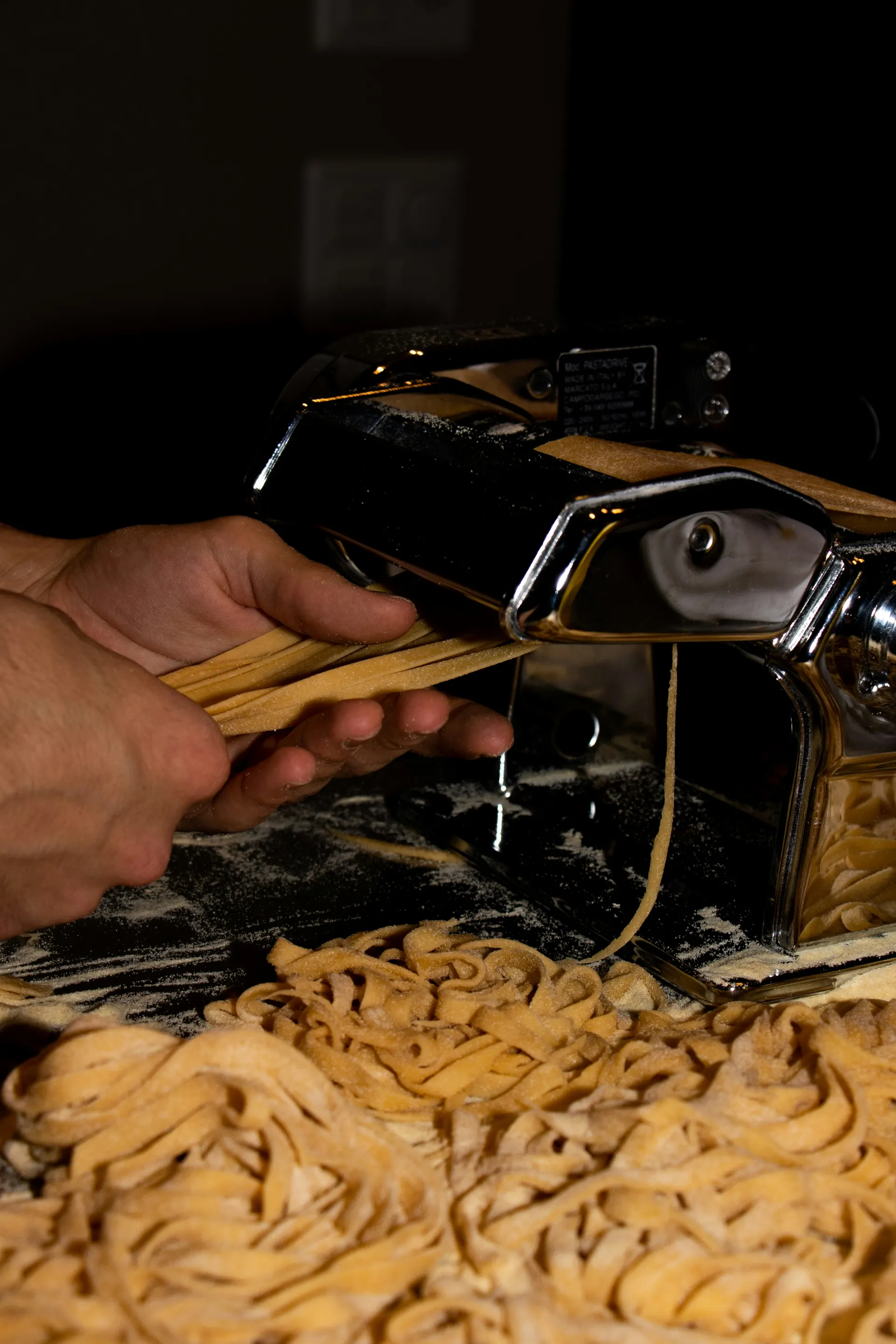 Fresh pasta dough passing through a hand-cranked pasta machine
