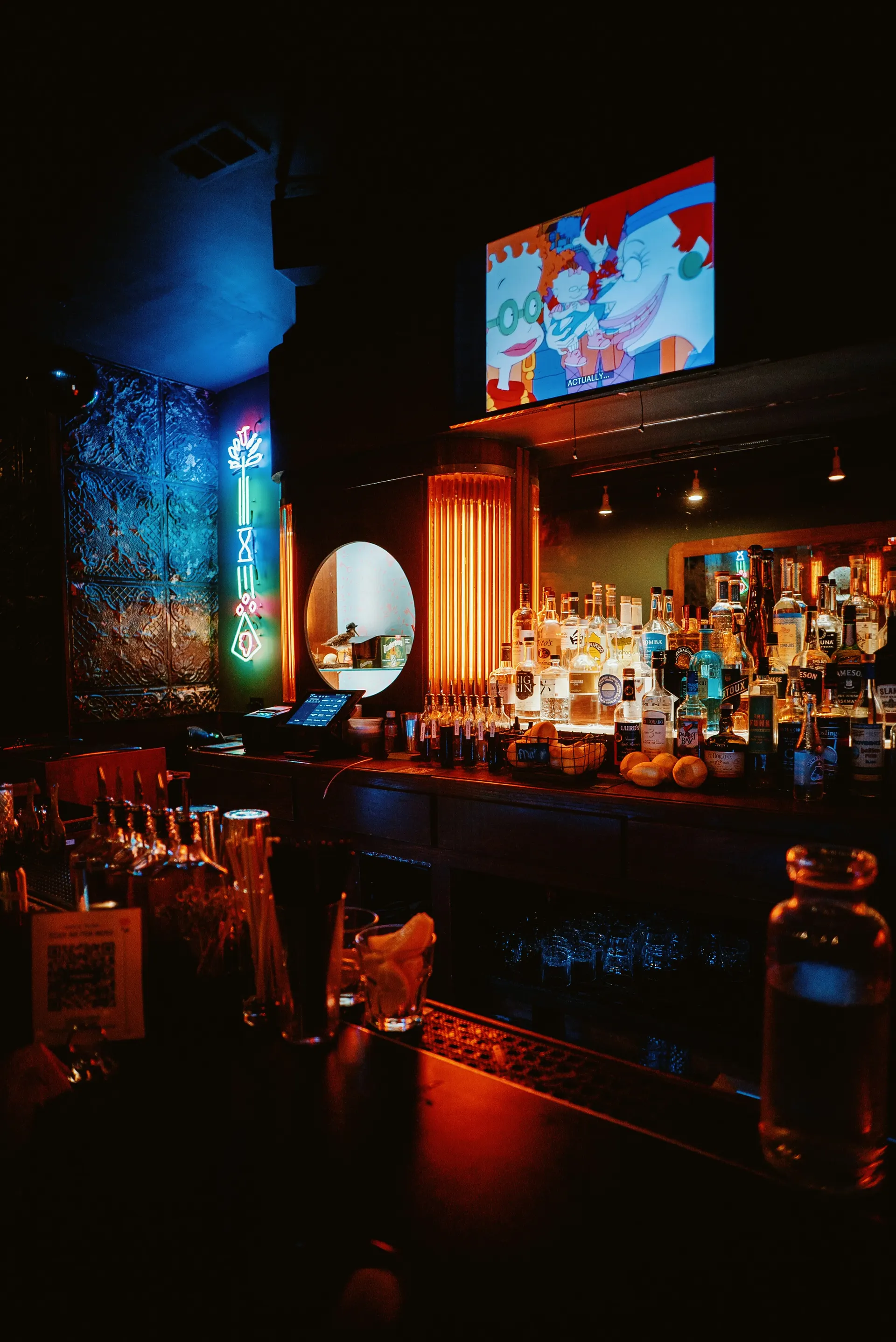 Liquor bottles and glassware glowing behind a dimly lit bar