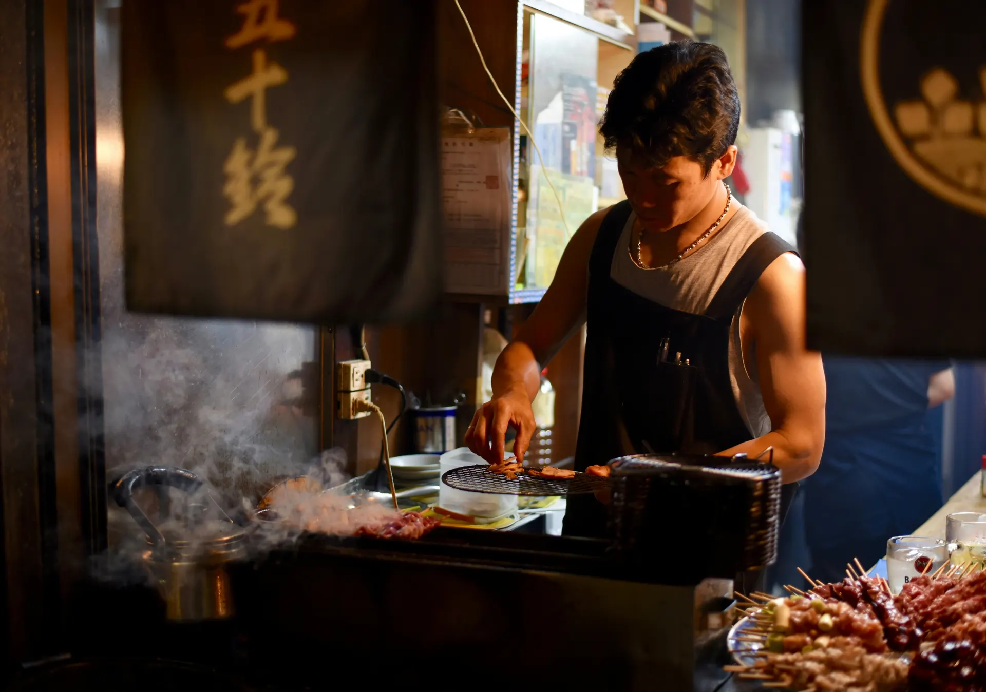 Cook tending a charcoal grill in a warm, smoky restaurant kitchen